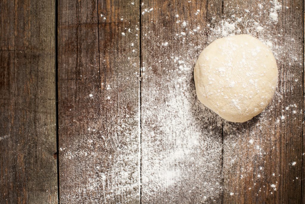 Traditional pizza dough, proved and ready to be made into a delicious stone baked pizza. On a rustic textured wooden background, dusted with flour