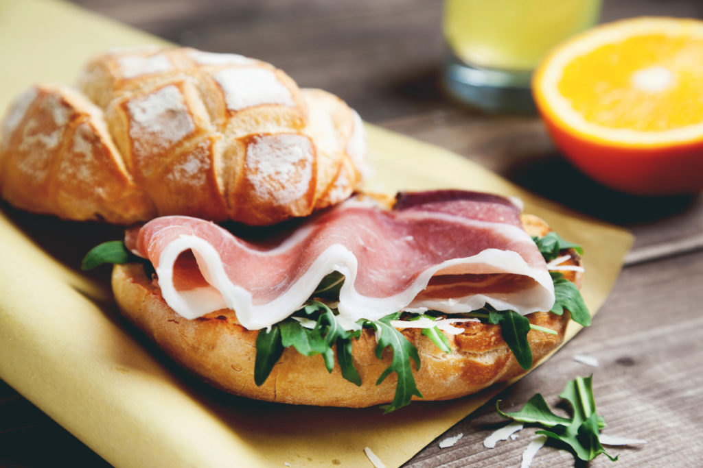 ciabatta bread prosciutto parmesan and arugula in paper with orange juice on background top view